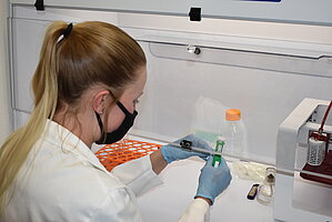 A women student works on test samples in a fume hood.